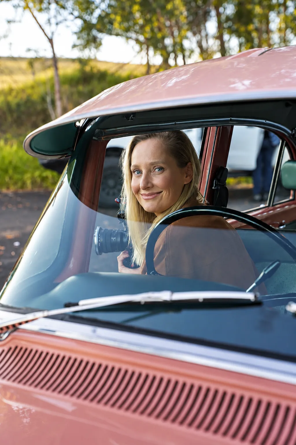Photographer smiling from the driver's seat of a vintage car, holding a camera