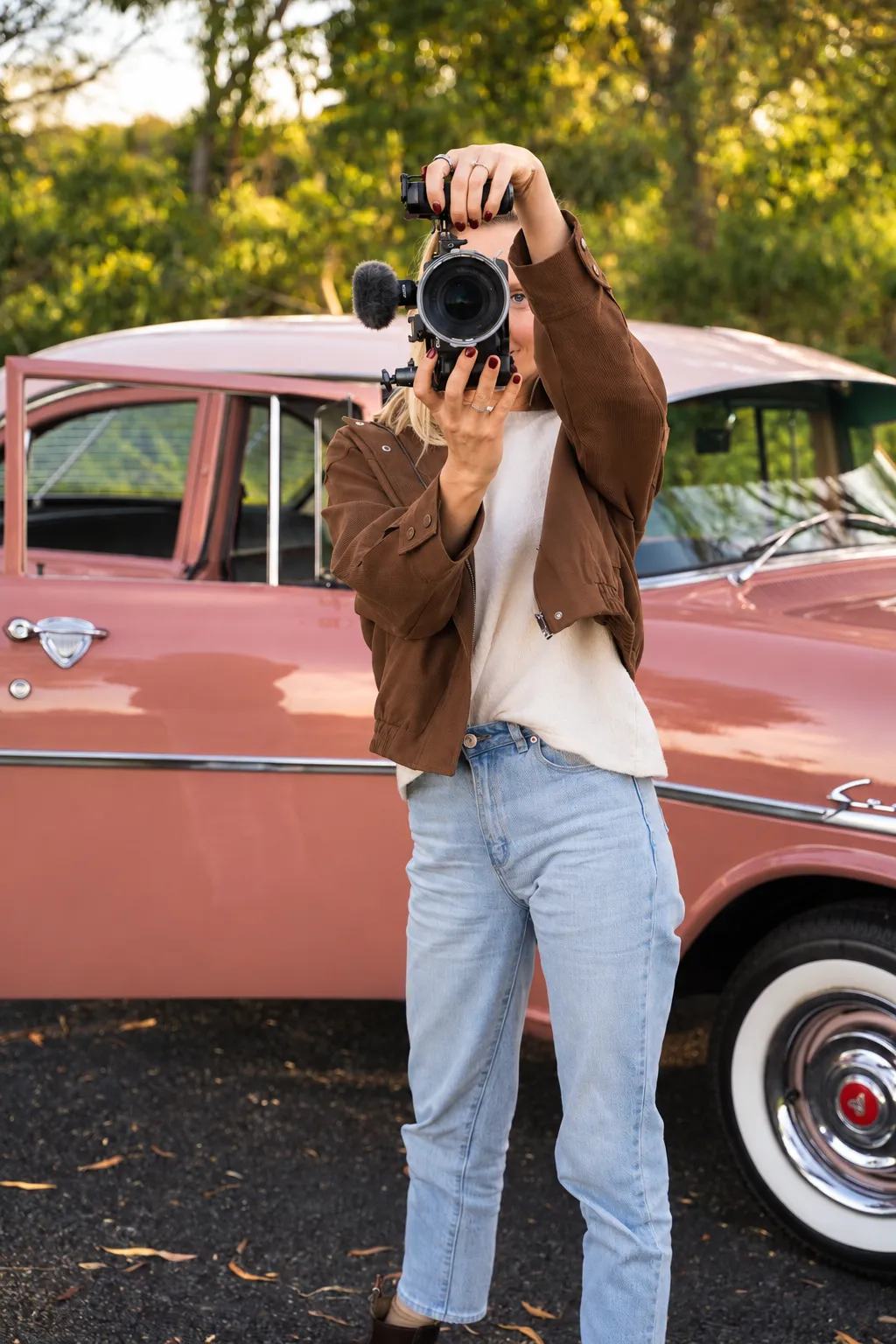 Content creator filming with a camera in front of a vintage car